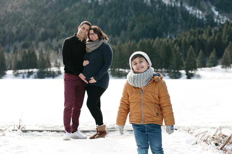 seance photo de grossesse dans la neige en hiver avec une famille qui joue et se fait des calins à la montagne près de Geneve 