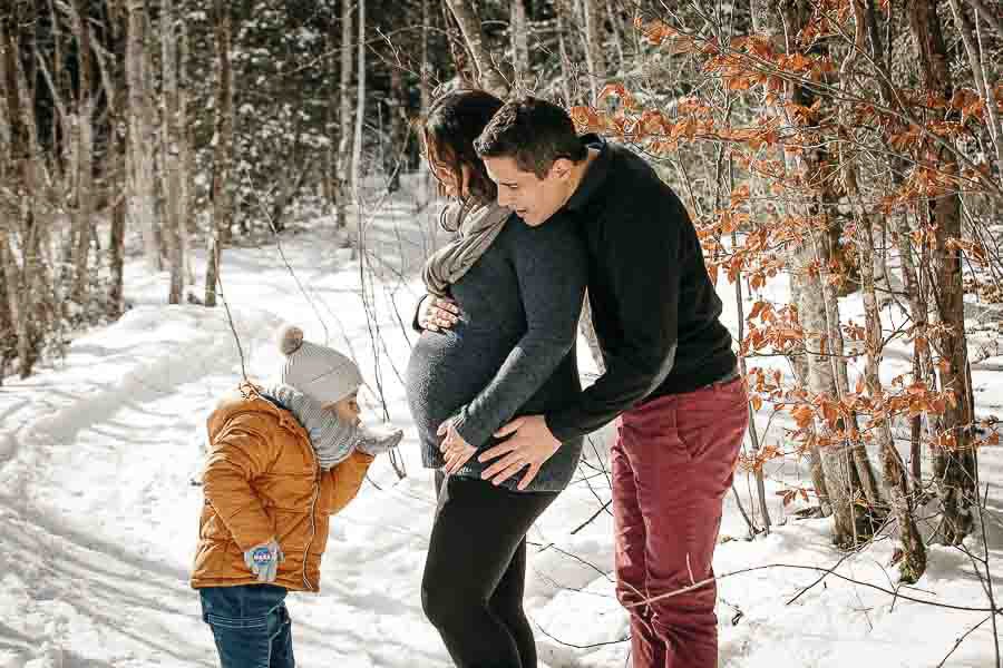 seance photo de grossesse dans la neige en hiver avec une famille qui joue et se fait des calins à la montagne près de Douvaine 