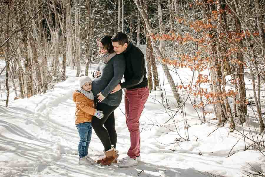 seance photo de grossesse dans la neige en hiver avec une famille qui joue et se fait des calins à la montagne près de Thonon 
